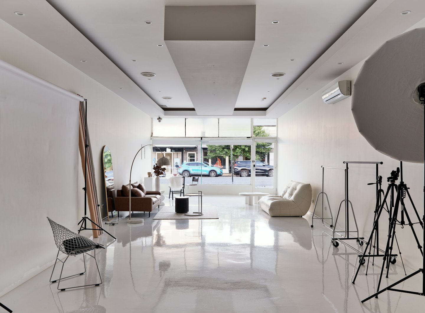Modernes Fotostudio mit Möbeln und Kleiderständern vor Fenstern.